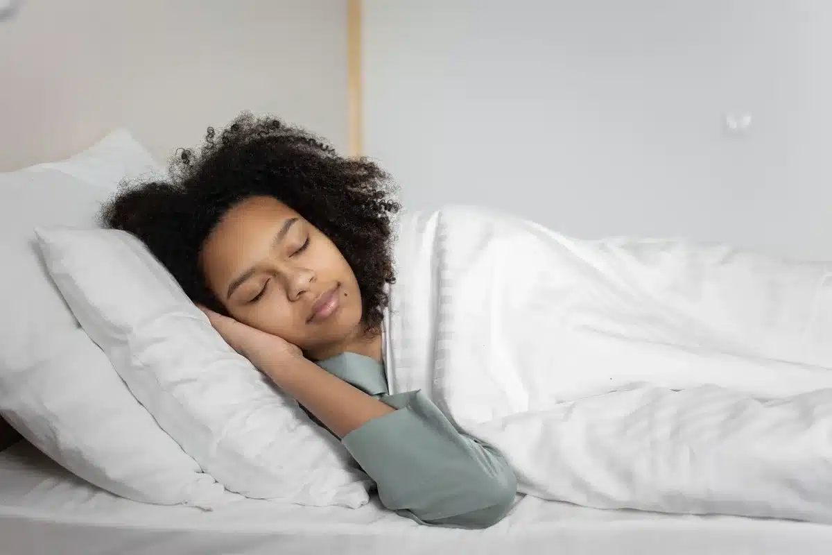 Une personne endormie paisiblement dans un lit confortable, illustrant les bonnes habitudes de sommeil.