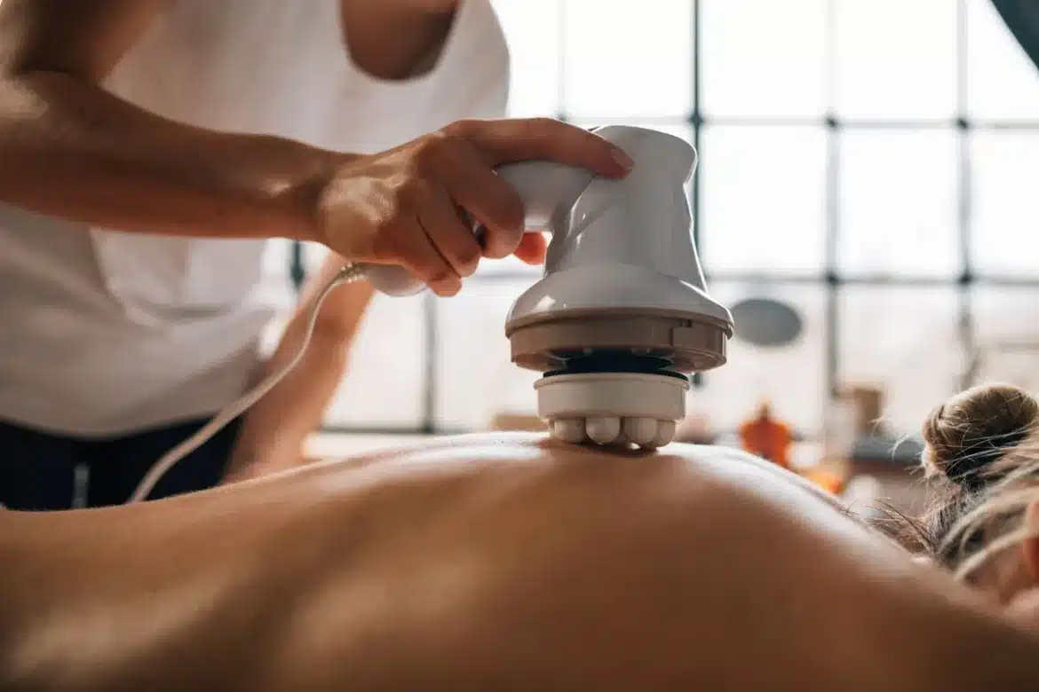 Mains pratiquant un massage à l'aide d'outils en bois sur une zone du corps dans un cadre spa relaxant.