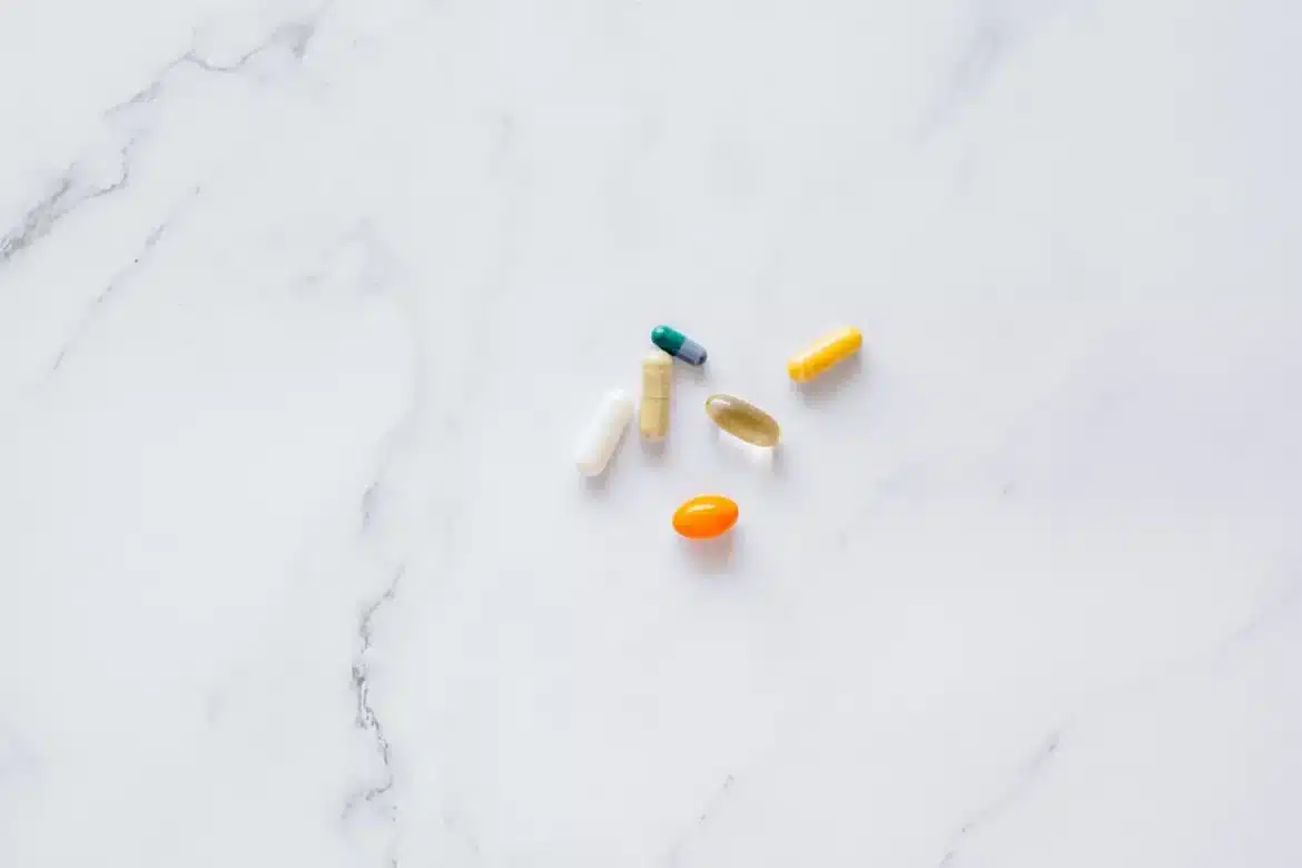 Main tenant différentes capsules et comprimés de compléments alimentaires à côté de légumes frais