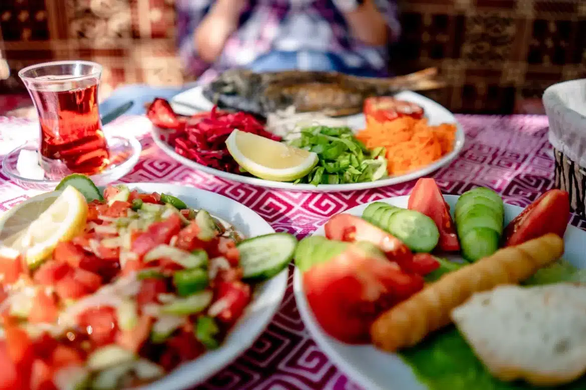 Assiette méditerranéenne avec légumes colorés, céréales complètes, poisson et huile d'olive sur table en bois.