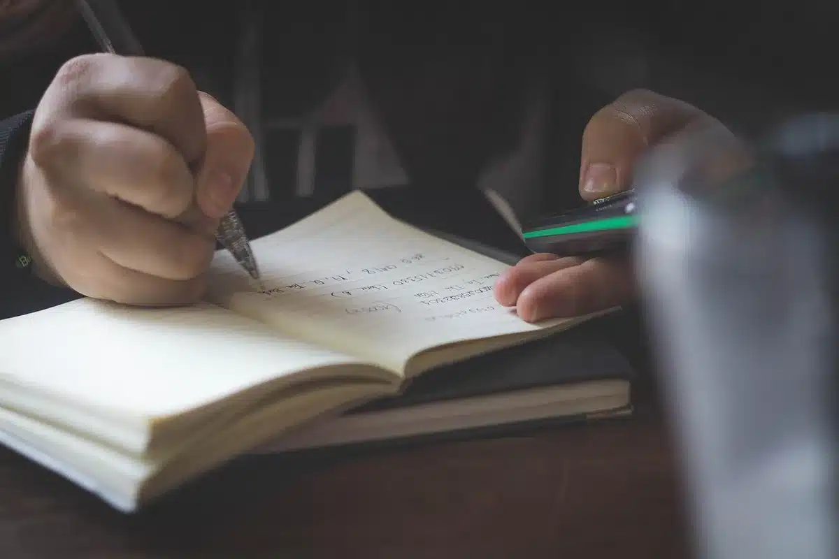 Main écrivant dans un petit journal sur l'appétit et l'humeur à une table ensoleillée